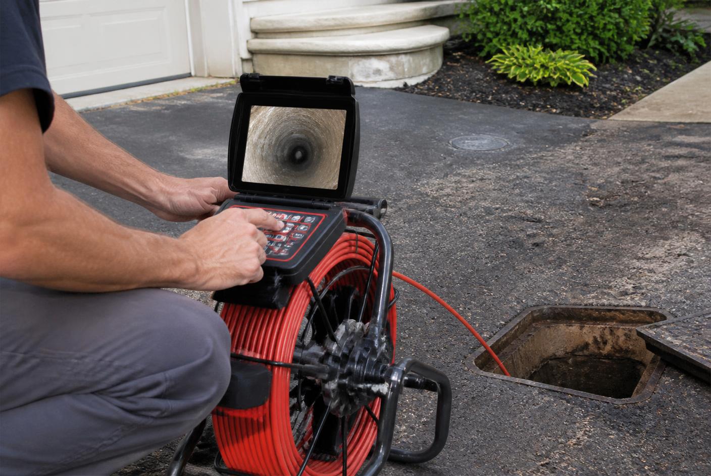 Technician reviewing sewer camera footage on a monitor beside an access pit